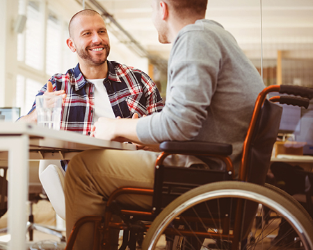 Ein Mann mit Rollstuhl und ein Mann ohne Rollstuhl sitzen gemeinsam an einem Tisch