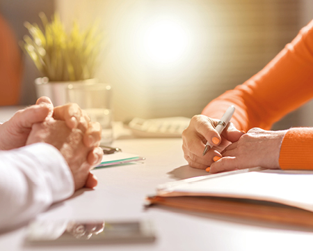 Hände von zwei Personen auf einem Arbeitstisch, mit Stift in der Hand